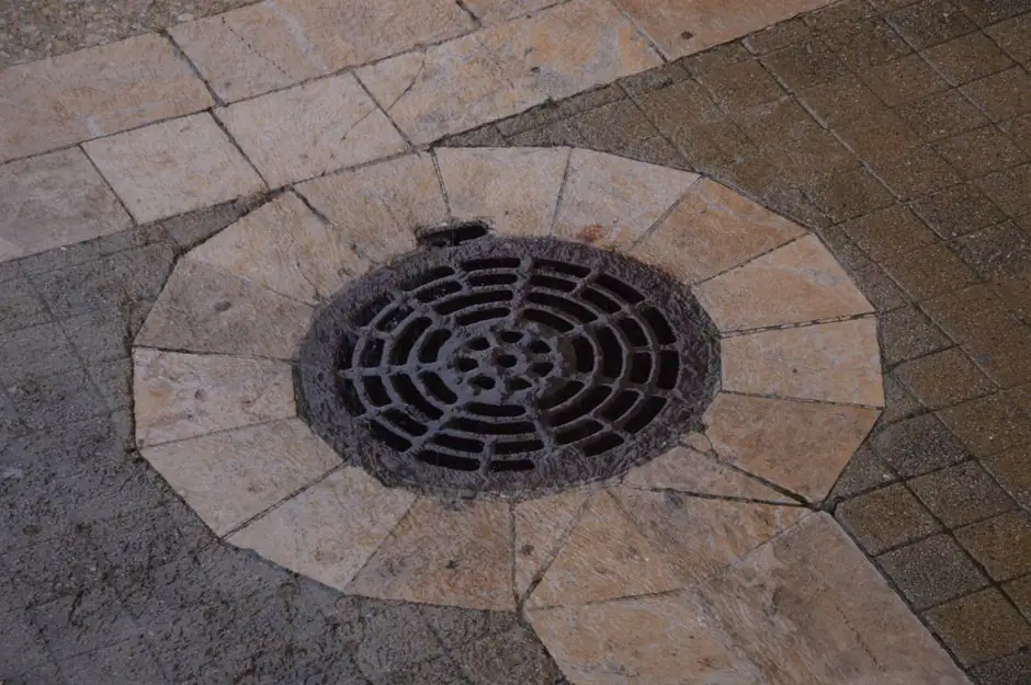 Close-up of an intricate iron manhole cover on a paved urban sidewalk.